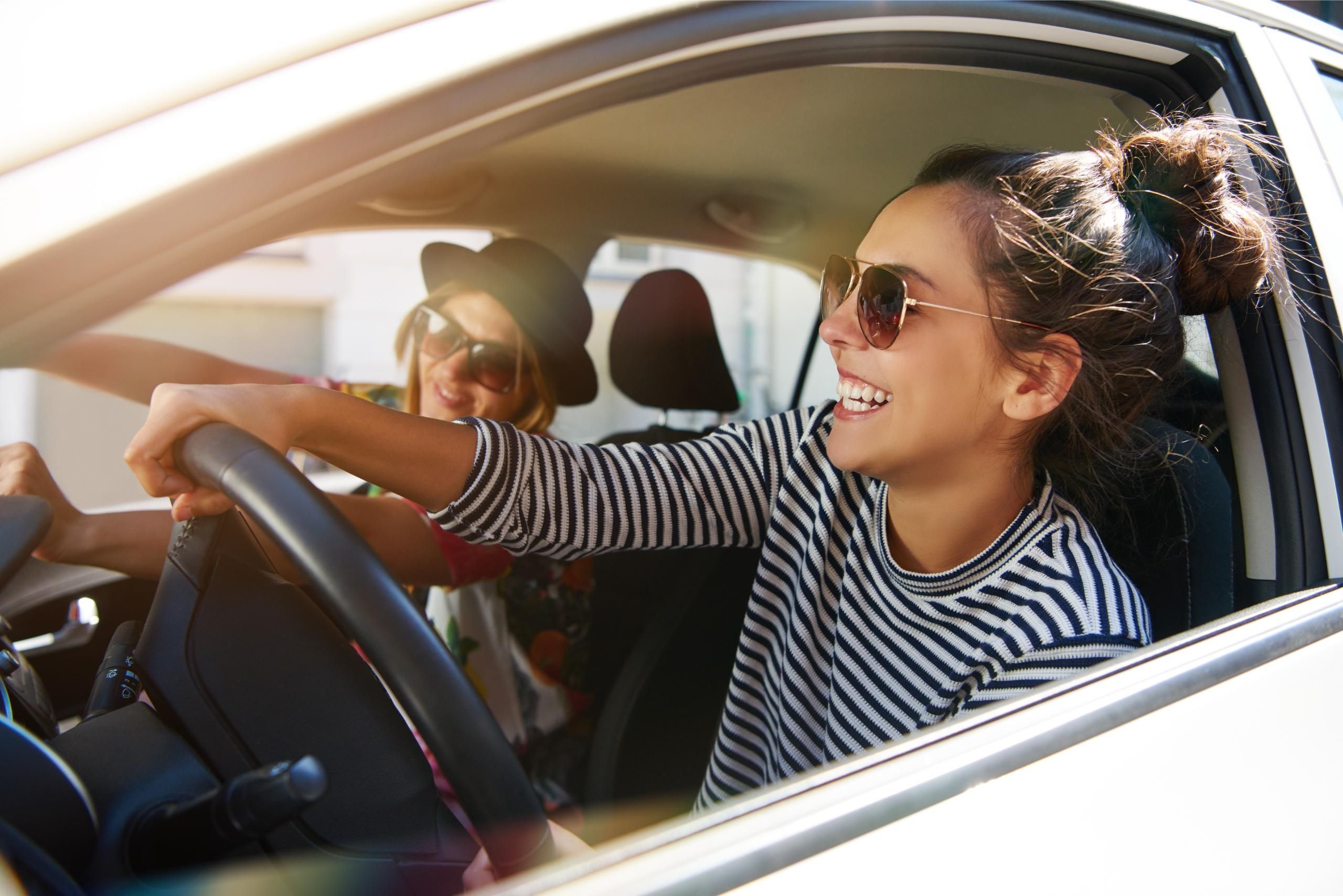 Zwei junge lachende Frauen mit Sonnenbrillen im Auto bei einer gemeinsamen Fahrt